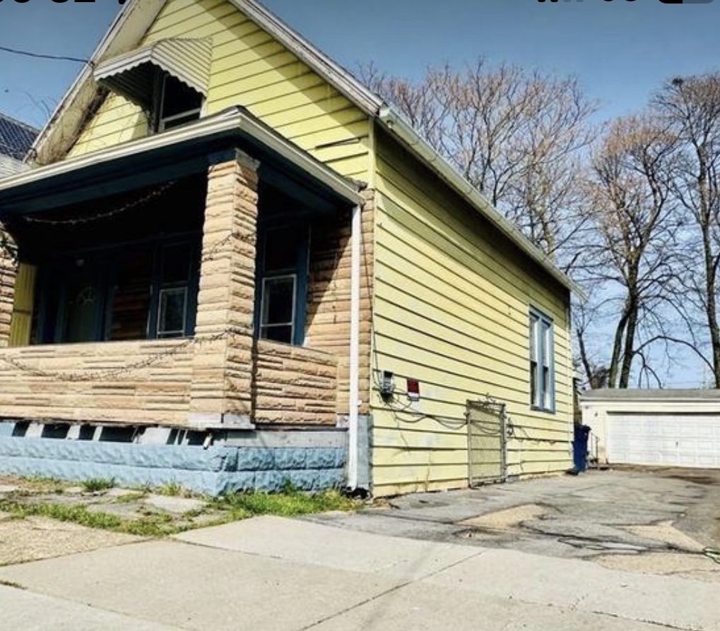 Yellow house with a stone pillared porch and detached garage in Buffalo, New York